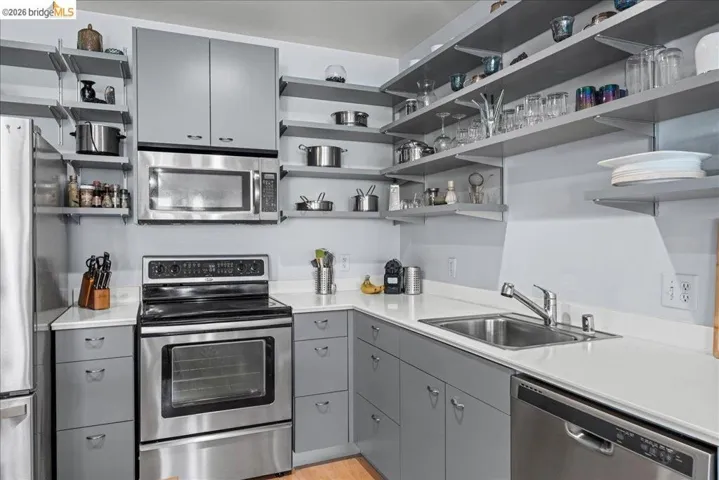 Kitchen with gray cabinets, stainless steel appliances, open shelves, and light countertops