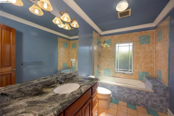 Full bath featuring tiled shower / bath, light tile patterned floors, vanity, and ornamental molding