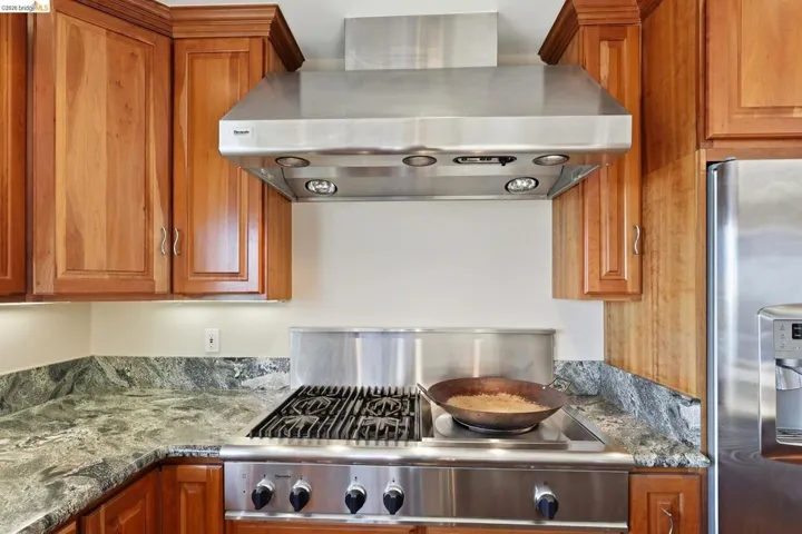 Kitchen with stainless steel appliances, wood finish cabinetry, and dark stone countertops