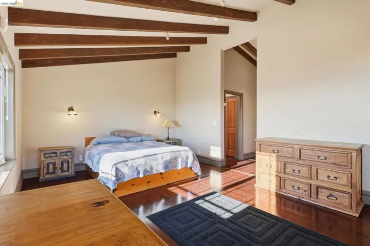Bedroom featuring dark wood-style floors and vaulted ceiling with beams