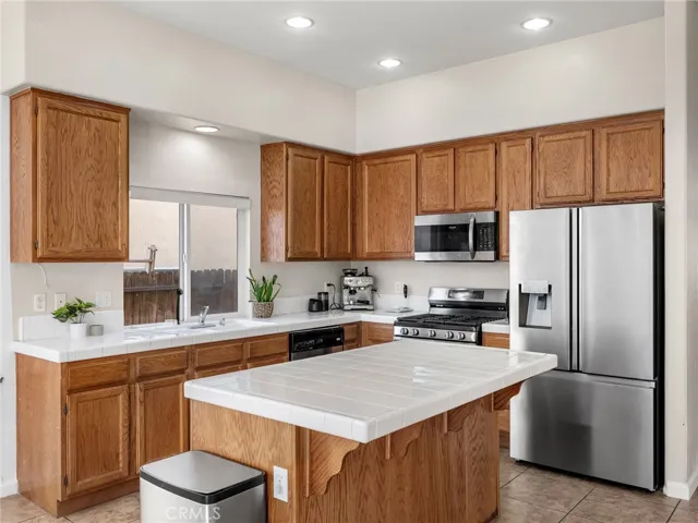 Generous kitchen with center island, ample cabinetry, stainless steel appliances, and tile countertops.