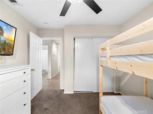This comfortable bedroom features carpeting, a ceiling fan for added comfort, and a spacious closet offering both functionality and a cozy retreat.