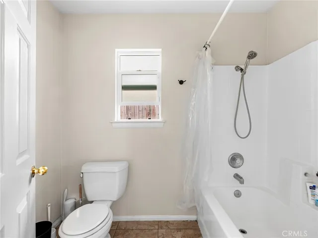 Clean and bright secondary bathroom featuring tile flooring, shower/tub combo, updated showerhead, and natural light from privacy window.