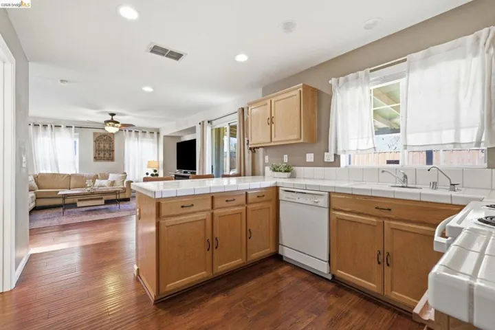 Kitchen featuring tile counters, white dishwasher, open floor plan, dark wood-type flooring, and recessed lighting