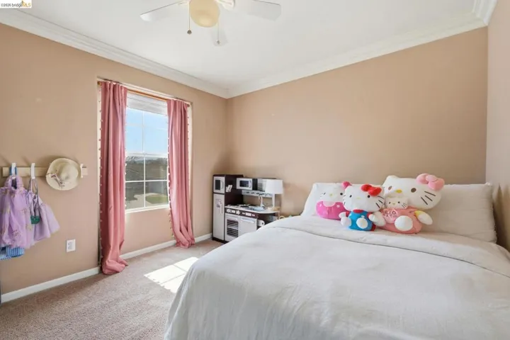 Bedroom with ceiling fan, light colored carpet, and ornamental molding