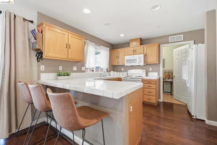 Kitchen featuring light wood finish cabinetry, a breakfast bar, a peninsula, tile countertops, and white appliances