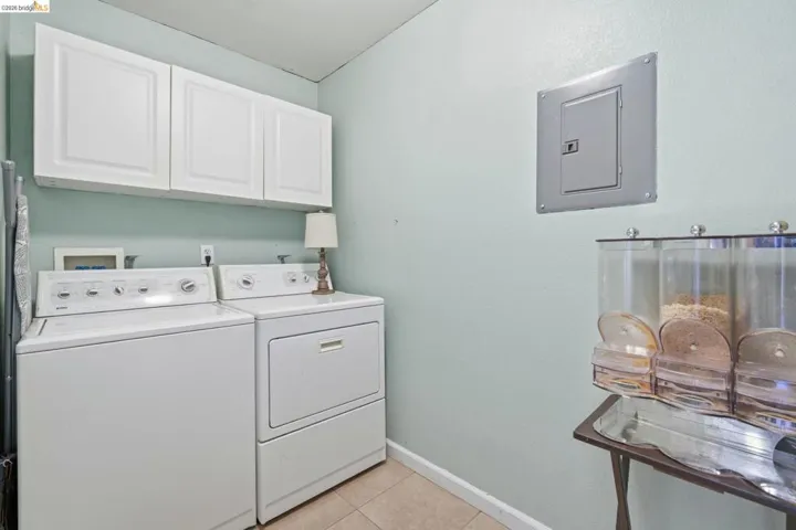 Laundry area next to kitchen with electric panel, cabinet space, light tile patterned floors
