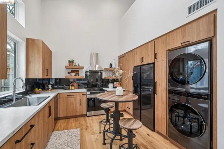 Kitchen featuring light wood finished floors, wood finish cabinetry, black fridge with ice dispenser, a high ceiling, and extractor fan