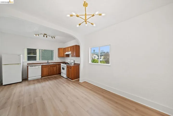 kitchen with wood finish cabinetry, white appliances, suspended lighting, light wood-type flooring, and arched walkways