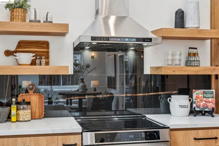 Kitchen featuring island exhaust hood, open shelves, decorative backsplash, and light stone countertops