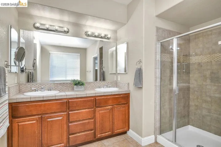 Bathroom with double vanity, a shower stall, a textured wall, light tile patterned floors, and backsplash
