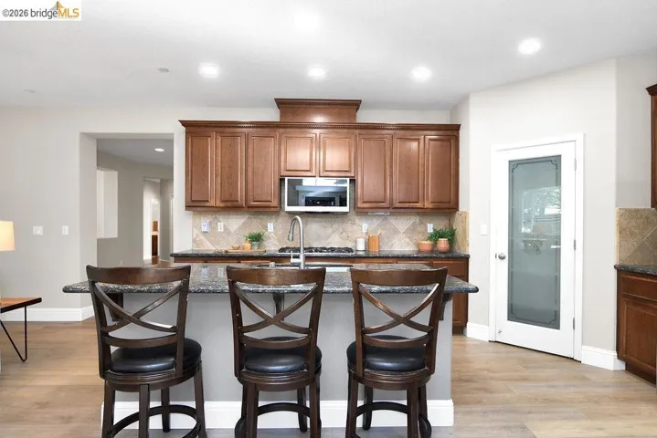 Kitchen with an island with sink, tasteful backsplash, a kitchen breakfast bar, dark stone counters, and recessed lighting