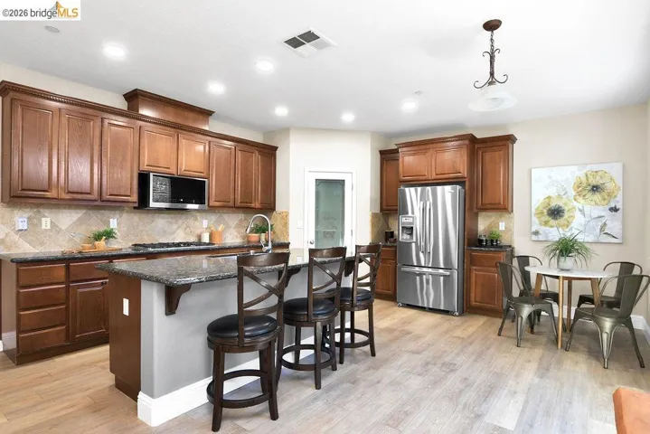 Kitchen featuring a breakfast bar, stainless steel appliances, an island with sink, light wood-style flooring, and pendant lighting