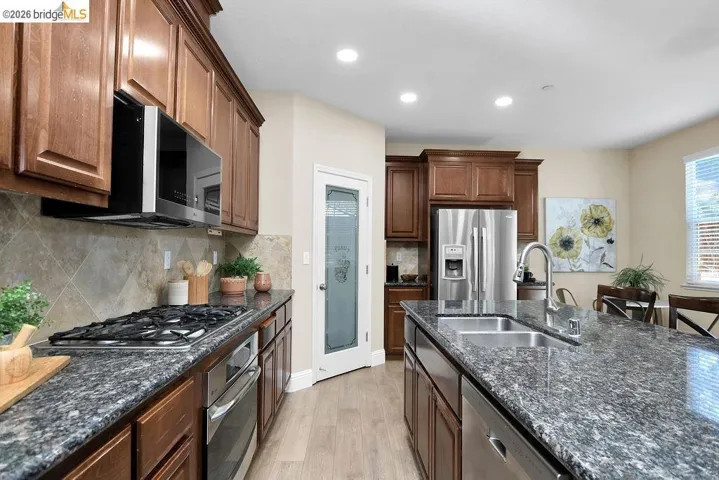 Kitchen featuring dark stone counters, stainless steel appliances, light wood finished floors, tasteful backsplash, and recessed lighting