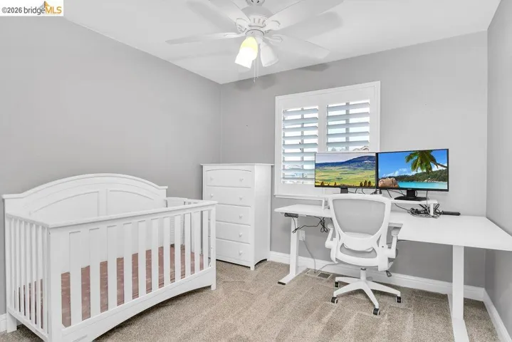 Bedroom with light carpet, a ceiling fan, a crib, and a desk