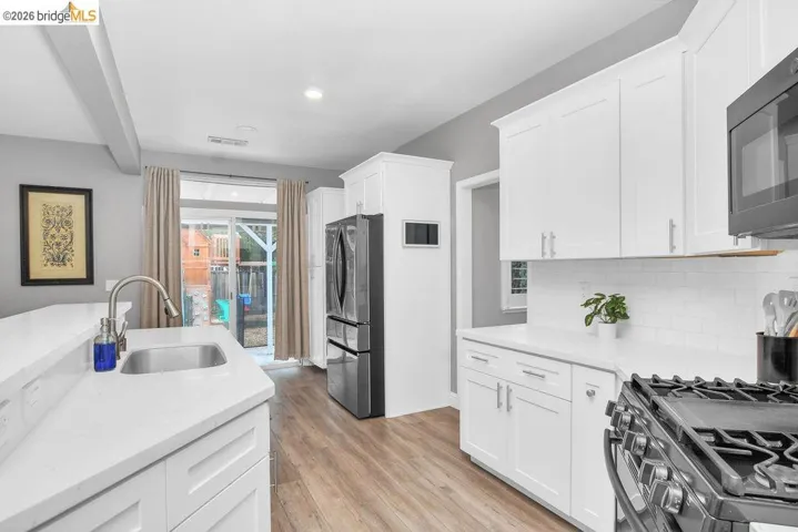 Kitchen with stainless steel appliances, light stone countertops, white cabinetry, and light wood finished floors