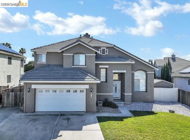 Traditional home featuring driveway, stucco siding, a tiled roof, a garage, and a chimney