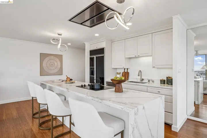 Kitchen with white cabinets, light stone counters, a kitchen bar, dark wood-type flooring, and a center island with sink