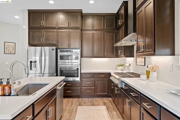 Kitchen featuring stainless steel appliances, dark wood finish cabinetry, light wood finished floors, and light stone counters