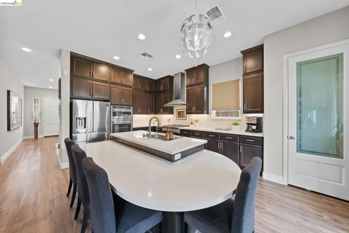 Kitchen featuring dark wood finish cabinetry, an island with sink, light wood-style floors, and stainless steel appliances