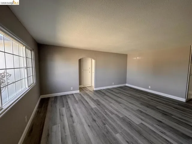 Unfurnished room featuring arched walkways, light wood finished floors, and a textured ceiling