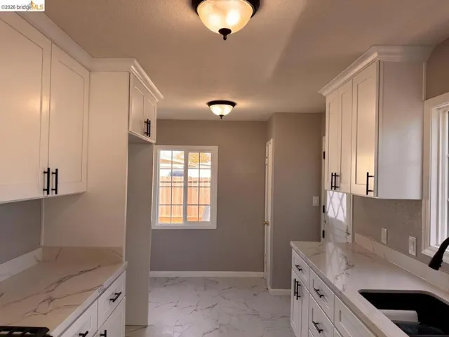 Kitchen with white cabinets, light marble finish flooring, and light stone counters