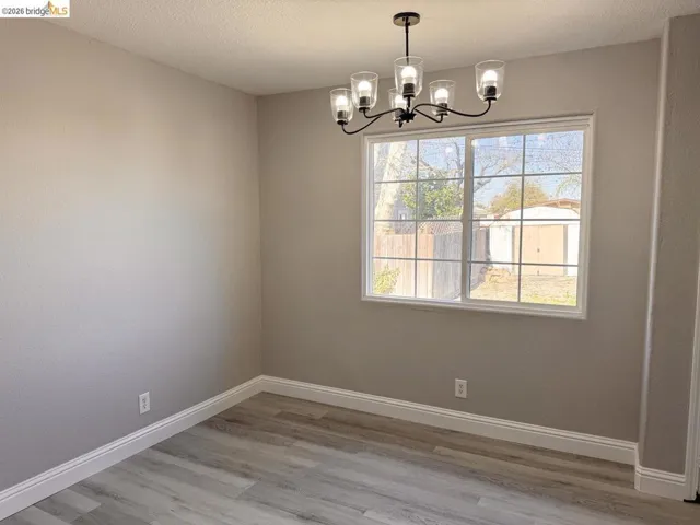Empty room with light wood-style flooring, hanging lights, and a textured ceiling