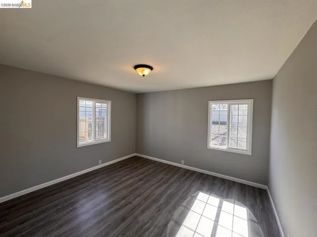 Empty room featuring dark wood-type flooring, plenty of natural light, and a textured ceiling
