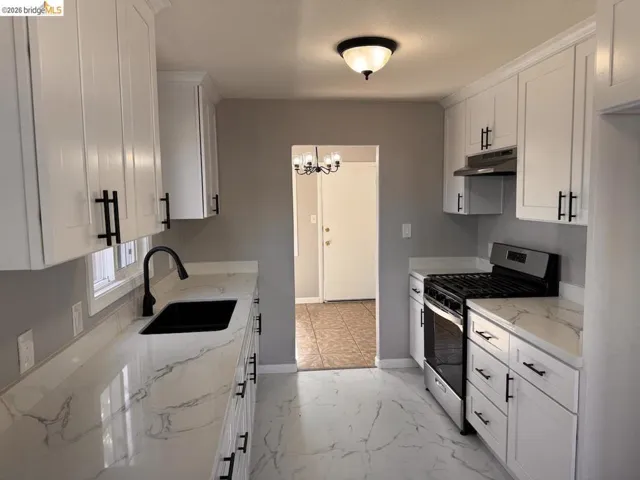 Kitchen with gas range, white cabinetry, light stone counters, light marble finish flooring, and hanging lights