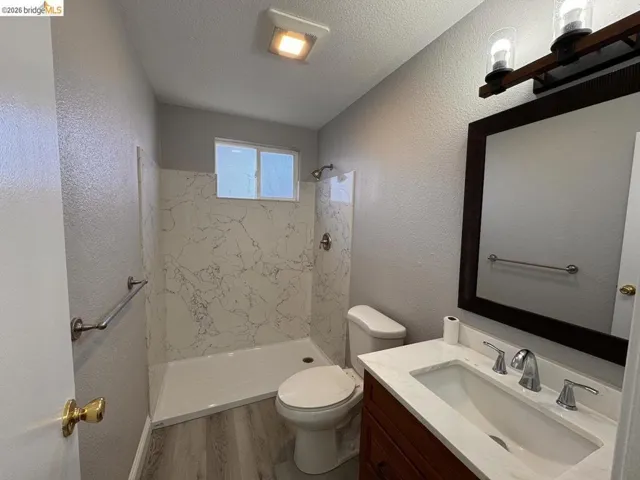 Full bathroom featuring a marble finish shower, vanity, a textured wall, wood finished floors, and a textured ceiling