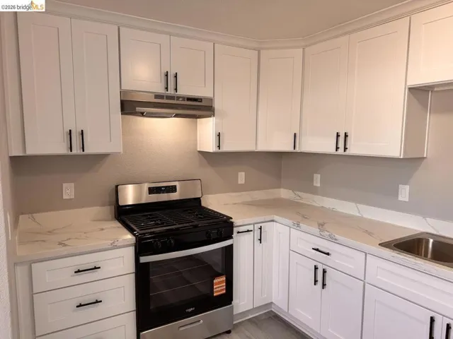 Kitchen with gas range, white cabinetry, light stone countertops, and a textured wall