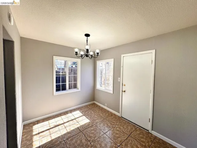 Unfurnished dining area featuring a textured ceiling, a chandelier, a textured wall, and tile patterned floors