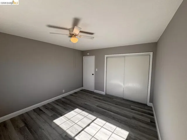Unfurnished bedroom with dark wood-style flooring, a closet, and a ceiling fan
