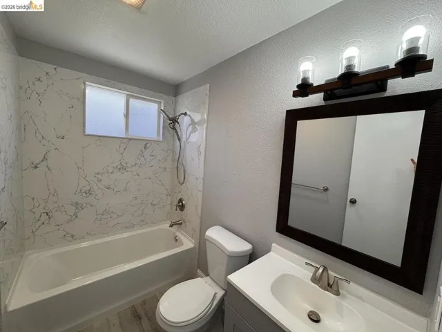 Bathroom with a textured wall, vanity, washtub / shower combination, and a textured ceiling
