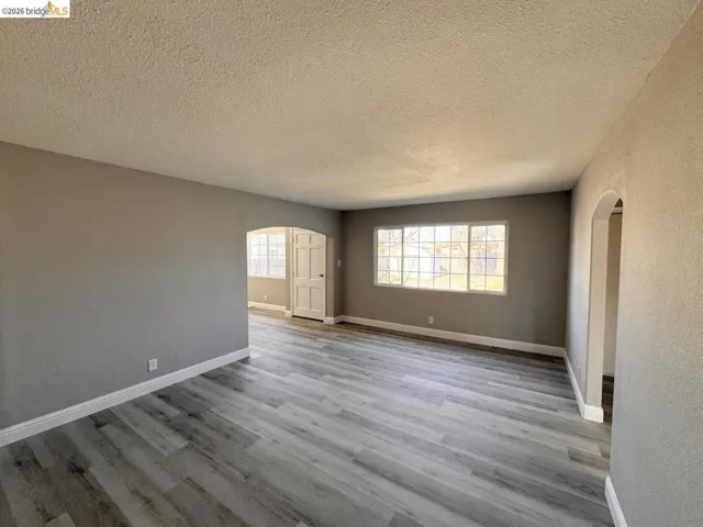 Unfurnished room with arched walkways, a textured ceiling, light wood-type flooring, and a textured wall