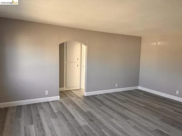 Unfurnished room with arched walkways, light wood-style flooring, and a textured ceiling