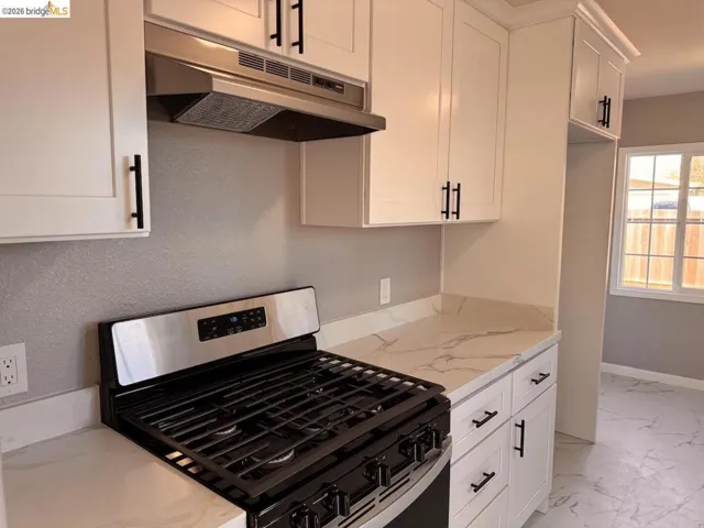 Kitchen featuring stainless steel gas range oven, white cabinetry, light stone countertops, and light marble finish flooring