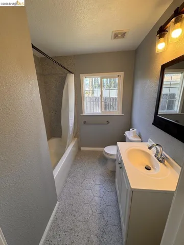 Bathroom with vanity, a textured wall, shower / bath combination with curtain, and a textured ceiling