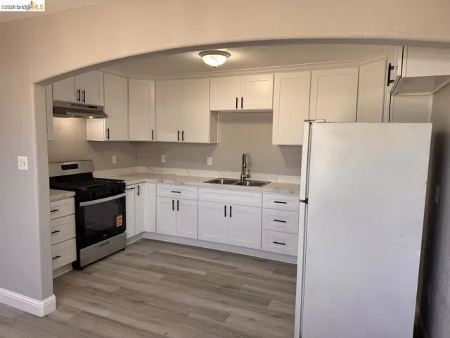 Kitchen with freestanding refrigerator, stainless steel gas range oven, white cabinets, and light wood-type flooring