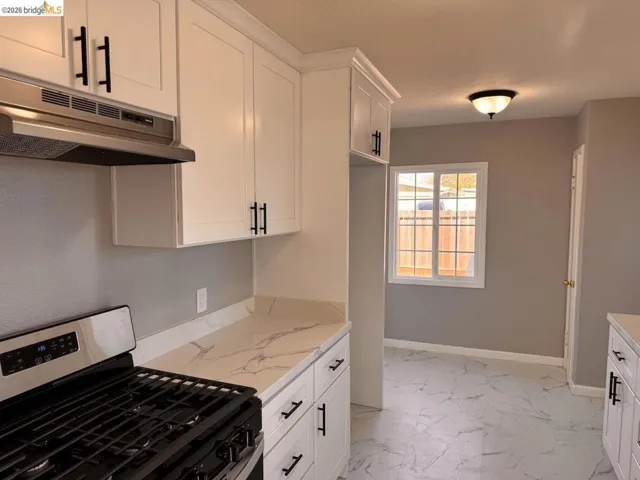 Kitchen with stainless steel gas range, white cabinets, and light marble finish floors