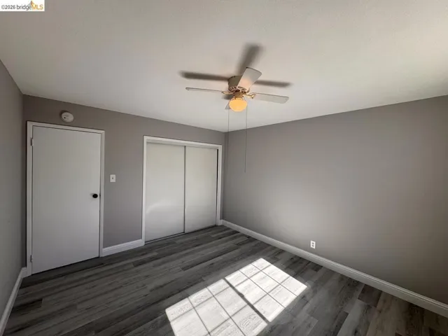 Unfurnished bedroom with dark wood-style flooring, a closet, and a ceiling fan