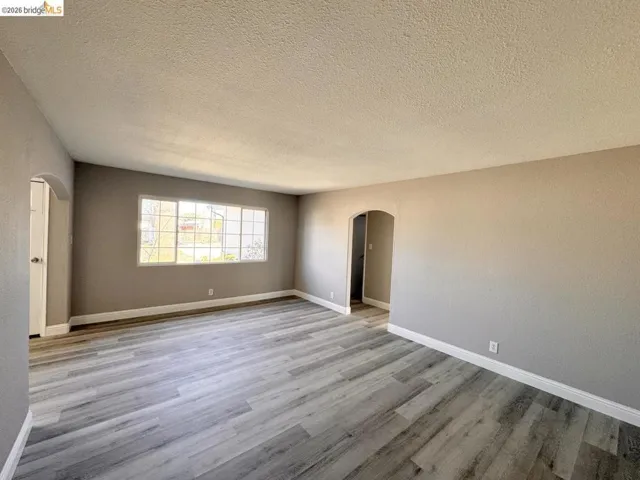 Spare room featuring arched walkways, light wood finished floors, and a textured ceiling