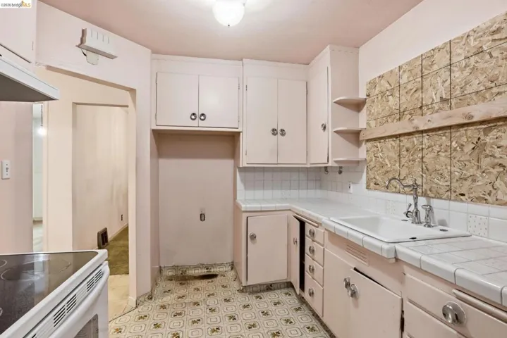 Kitchen featuring tile countertops, light flooring, open shelves, decorative backsplash, and white cabinetry