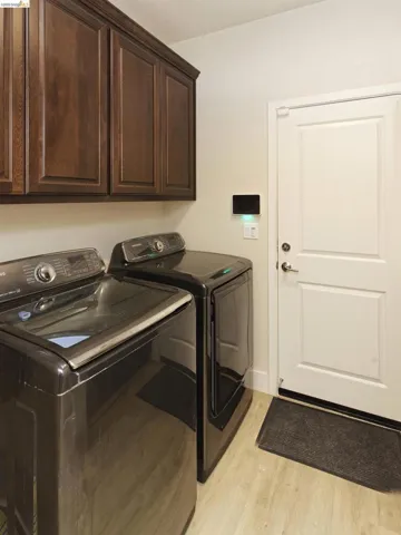 Laundry room with light wood-style floors, washer and clothes dryer, and cabinet space