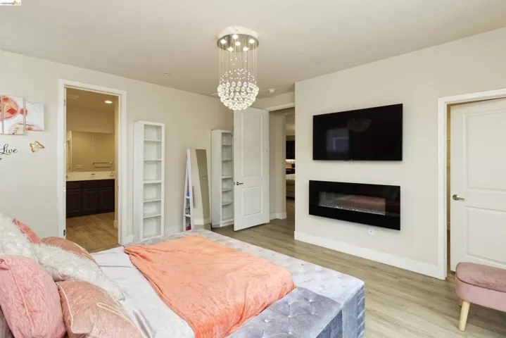 Bedroom featuring light wood-style floors, a chandelier, a glass covered fireplace, and ensuite bath
