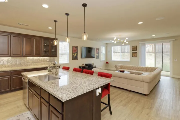 Kitchen with dark brown cabinets, a breakfast bar, light wood-style flooring, pendant lighting, and light stone countertops