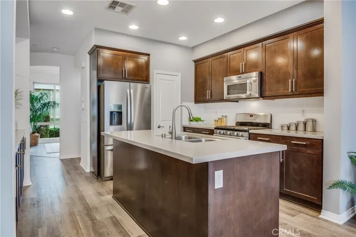 Beautiful and open concept kitchen with rich cabinetry pantry, quartz countertops, stainless appliances, wide plank flooring, counterop seating centered around the island