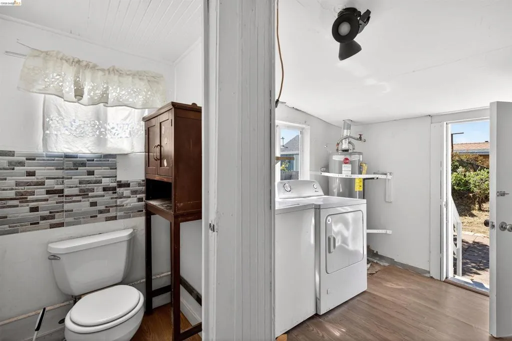 Laundry area with washer and dryer, water heater, wood-finish flooring, and exterior access