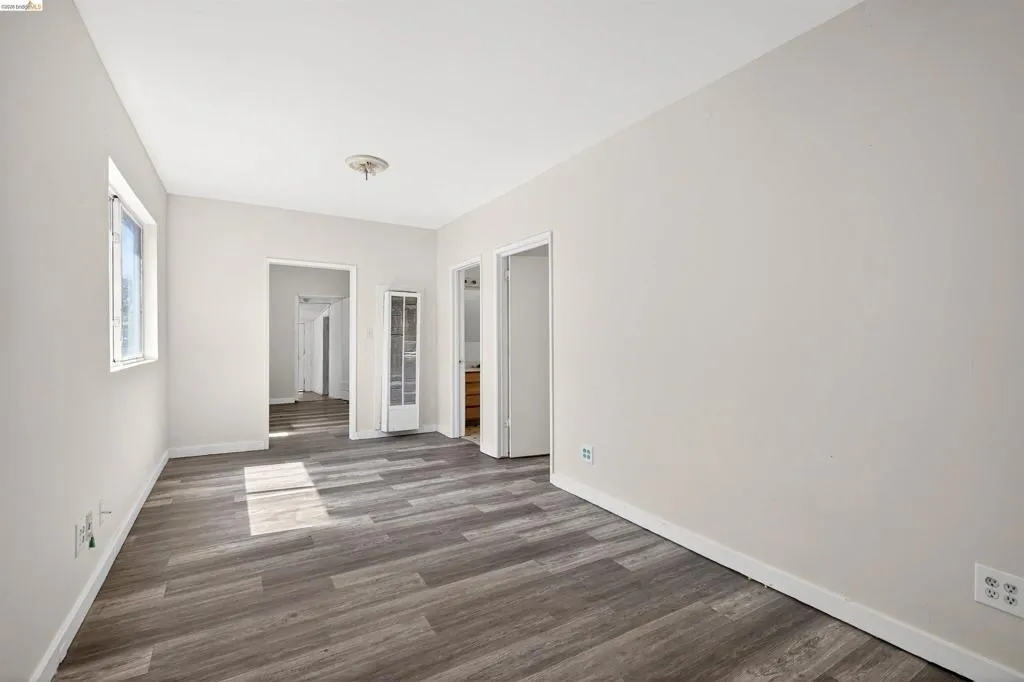 Spacious room featuring wood-finish flooring, light neutral wall paint, white trim, and a ceiling-mounted light fixture