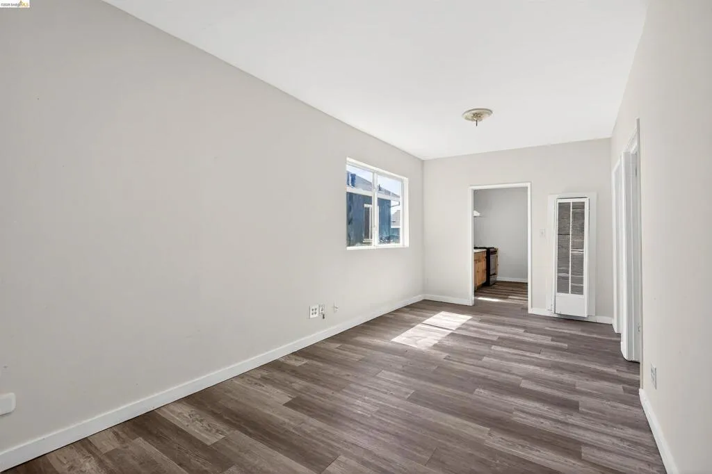 Spacious room featuring wood-finish flooring, white baseboards, and neutral wall tones
